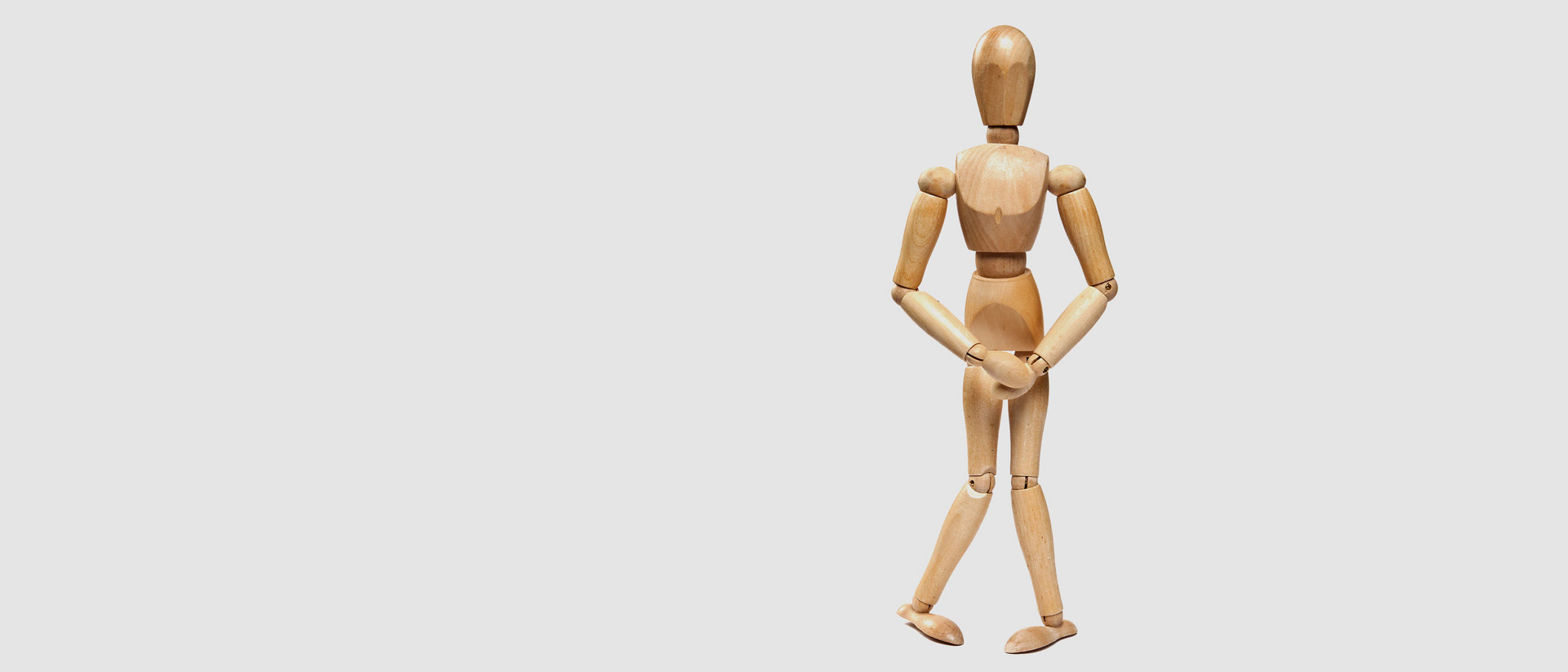 Ansicht einer Holzfigur in der typischen "Ich muss Pippi"-Pose mit gekreuzten Beinen und den Händen vor der Blase