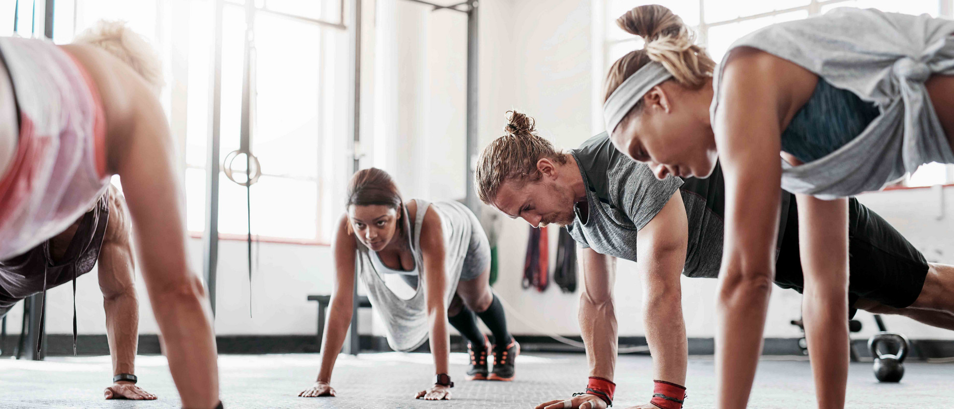 Fünf sportliche Menschen trainieren in einem hellen Studio mit ihrem eigenen Körpergewicht.