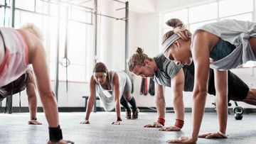 Fünf sportliche Menschen trainieren in einem hellen Studio mit ihrem eigenen Körpergewicht.