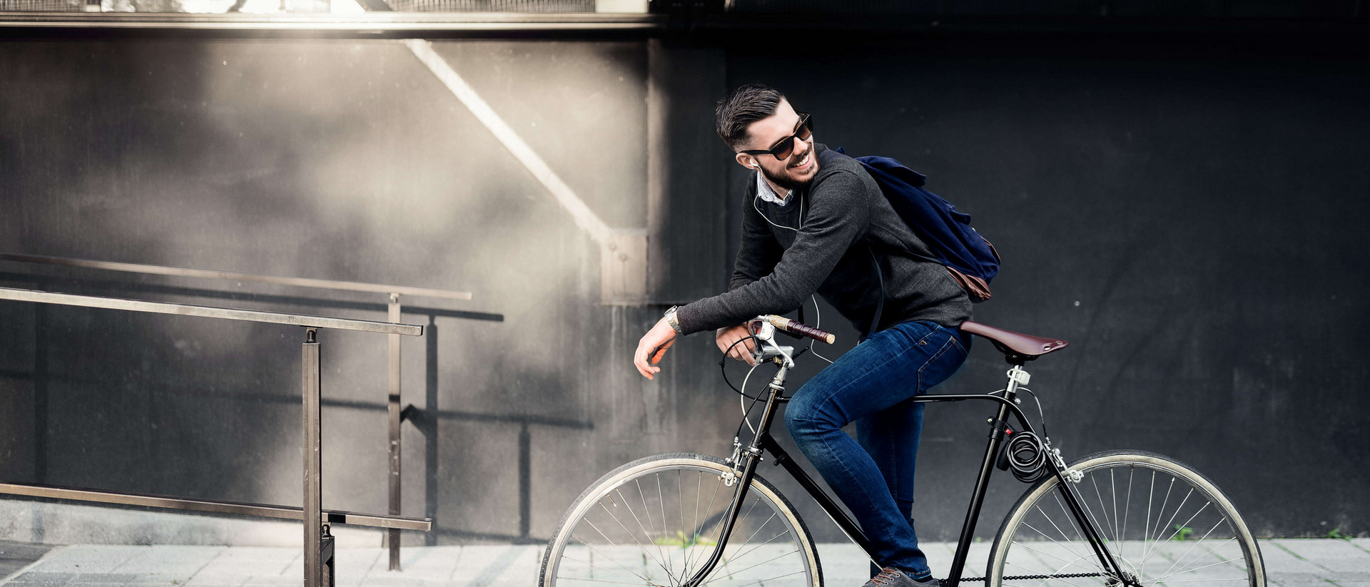 Ein junger Mann steht mit seinem Fahrrad vor einer Rampe. Er blickt hinter sich, als wenn er auf jemanden wartet.
