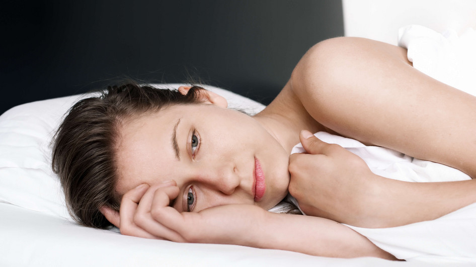 Eine junge Frau liegt im Bett und hat einen sehr besorgten oder unglücklichen Gesichtsausdruck.