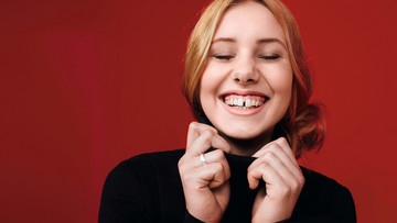 Eine junge Frau lacht mit geschlossenen Augen. Ihre Zahnlücke zwischen den Schneidezähnen ist dabei zu sehen.