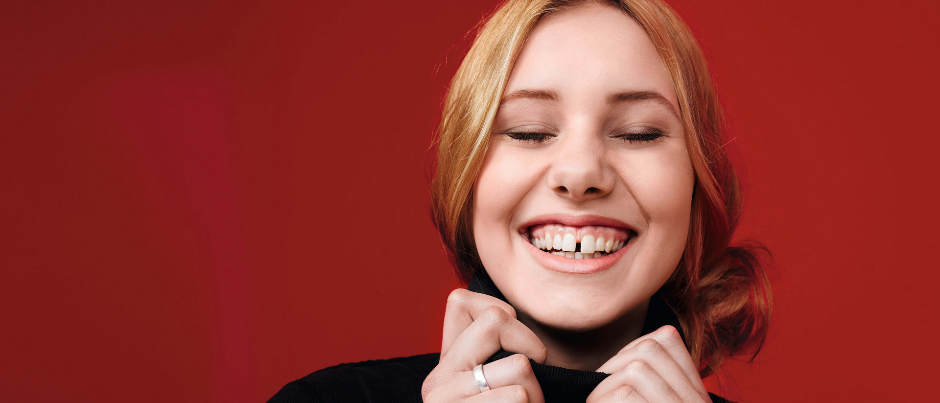 Eine junge Frau lacht mit geschlossenen Augen. Ihre Zahnlücke zwischen den Schneidezähnen ist dabei zu sehen.