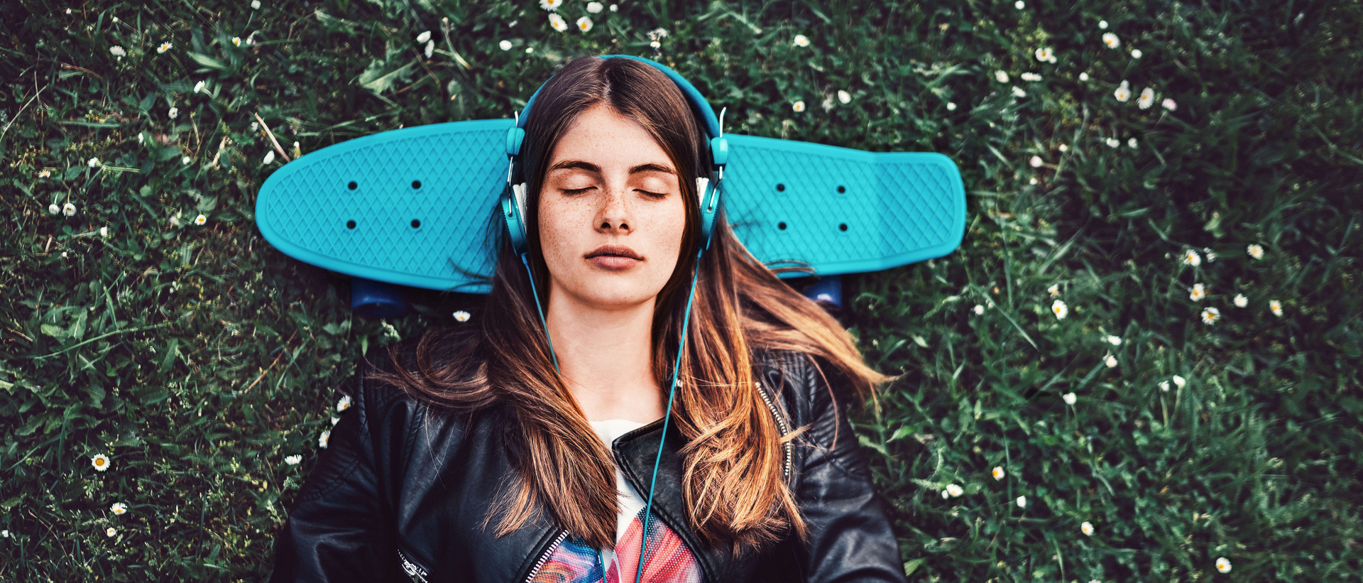 Junge Frau liegt mit geschlossenen Augen und Kopfhörern auf dem Kopf auf dem Rücken liegend im Gras