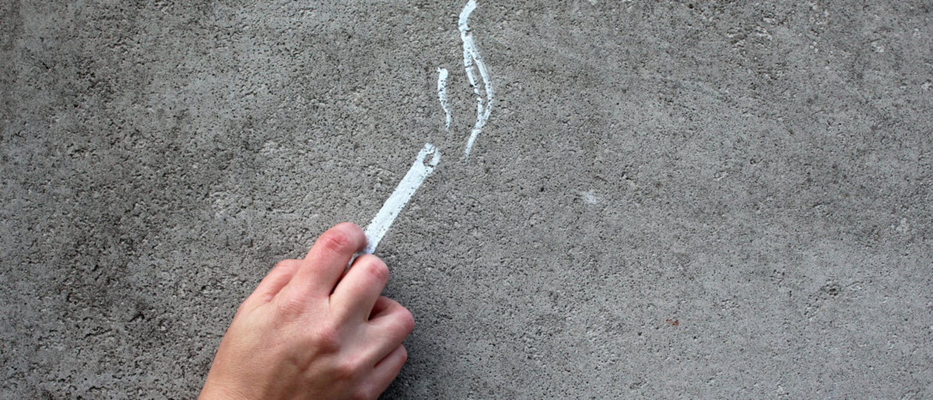 Auf einen grauen Asphaltboden ist eine weiße Zigarette gemalt. Eine Hand liegt auf dem Asphaltboden auf der Höhe der Zigarette, sodass es aussieht, als ob sie sie hält. 
