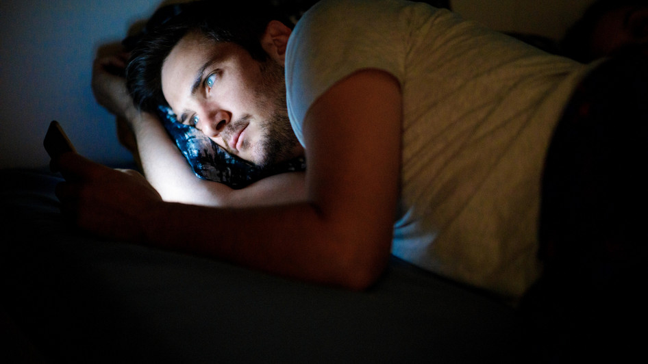 Mann schaut in seinem Bett im dunklen noch auf das Smartphone