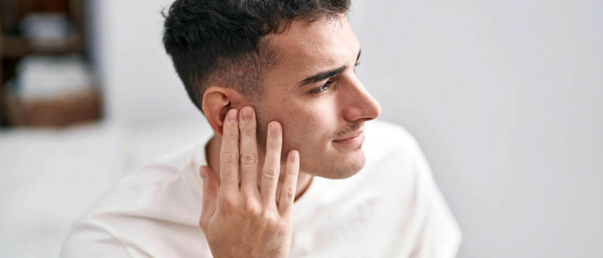 Ein junger Mann mit braunen Locken ist im Profil zu sehen. Er hält seine Hand an sein rechtes Ohr.