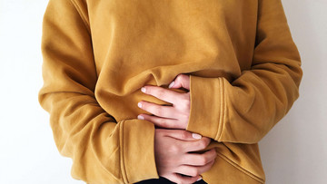 Ein Oberkörper, bekleidet mit einem ockerfarbenen Pullover, ist zu sehen. Der Mensch hält beide Hände vor den Bauch, so, als ob er sehr satt sei. 