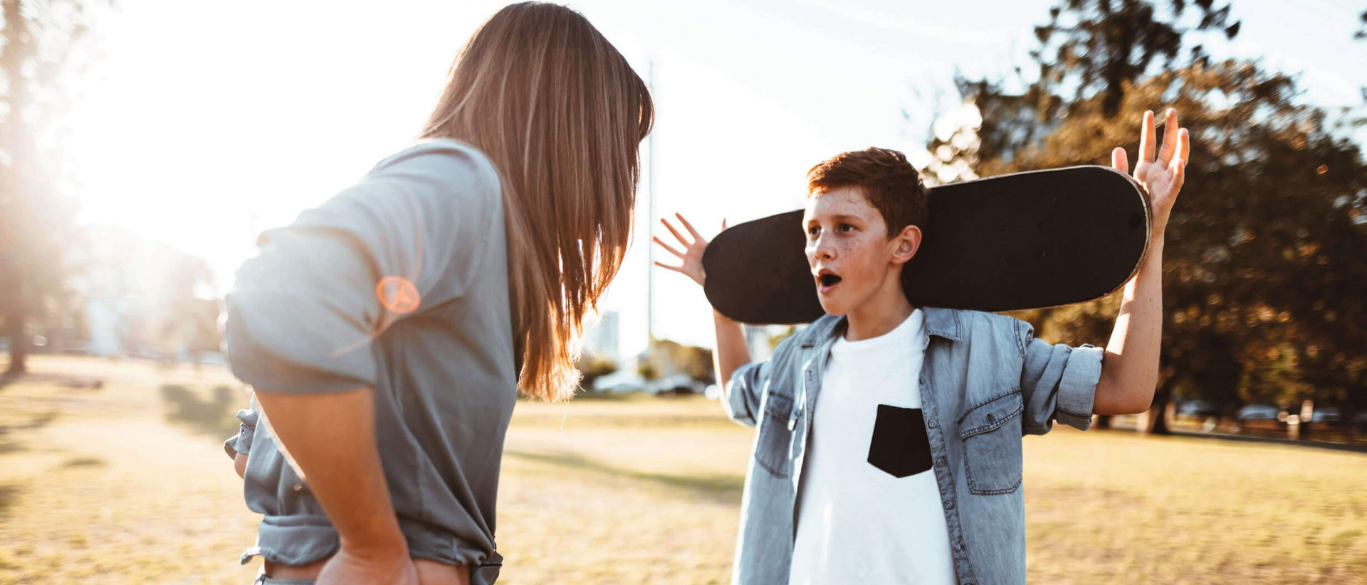 Ein junge und seine Mutter stehen sich gegenüber wie im Streit. Der junge trägt ein Skateboard auf seinen Schultern, die Mutter hat ihre Hände in die Hüften gestemmt.