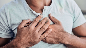 Brustkorb eines Mannes im hellgrauen T-Shirt mit Händen auf der Brust liegend