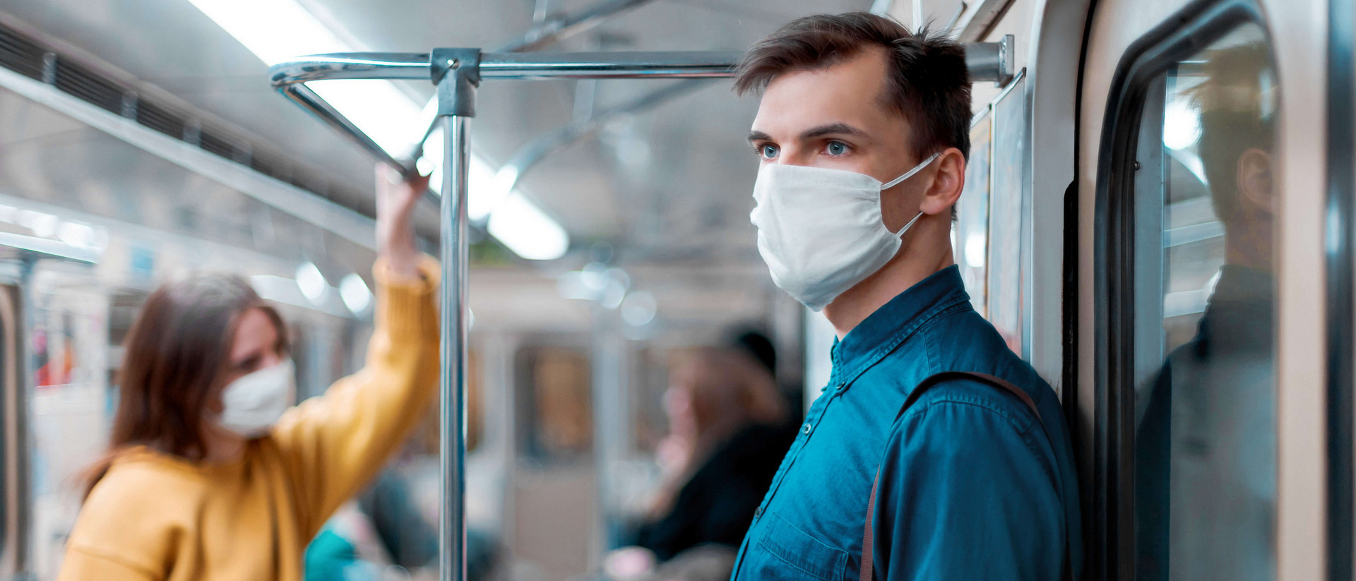 Ein Mann steht in einer U-Bahn, trägt eine Maske und hält ein Handy in der Hand. 