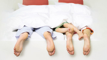 Füße von zwei Erwachsenen und einem Kleinkind luken unter der Bettdecke hervor