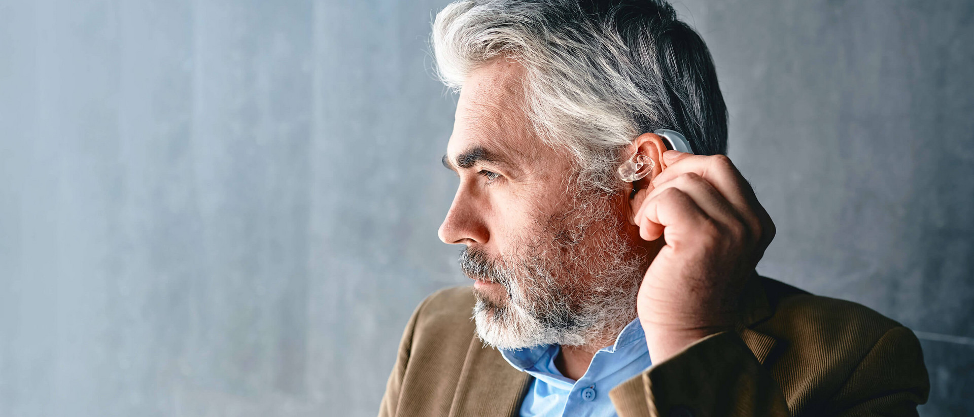 Ein Mann mit grauen Haaren und Drei-Tage-Bart ist im Profil zu sehen. In seinem linken Ohr trägt er ein Hörgerät.
