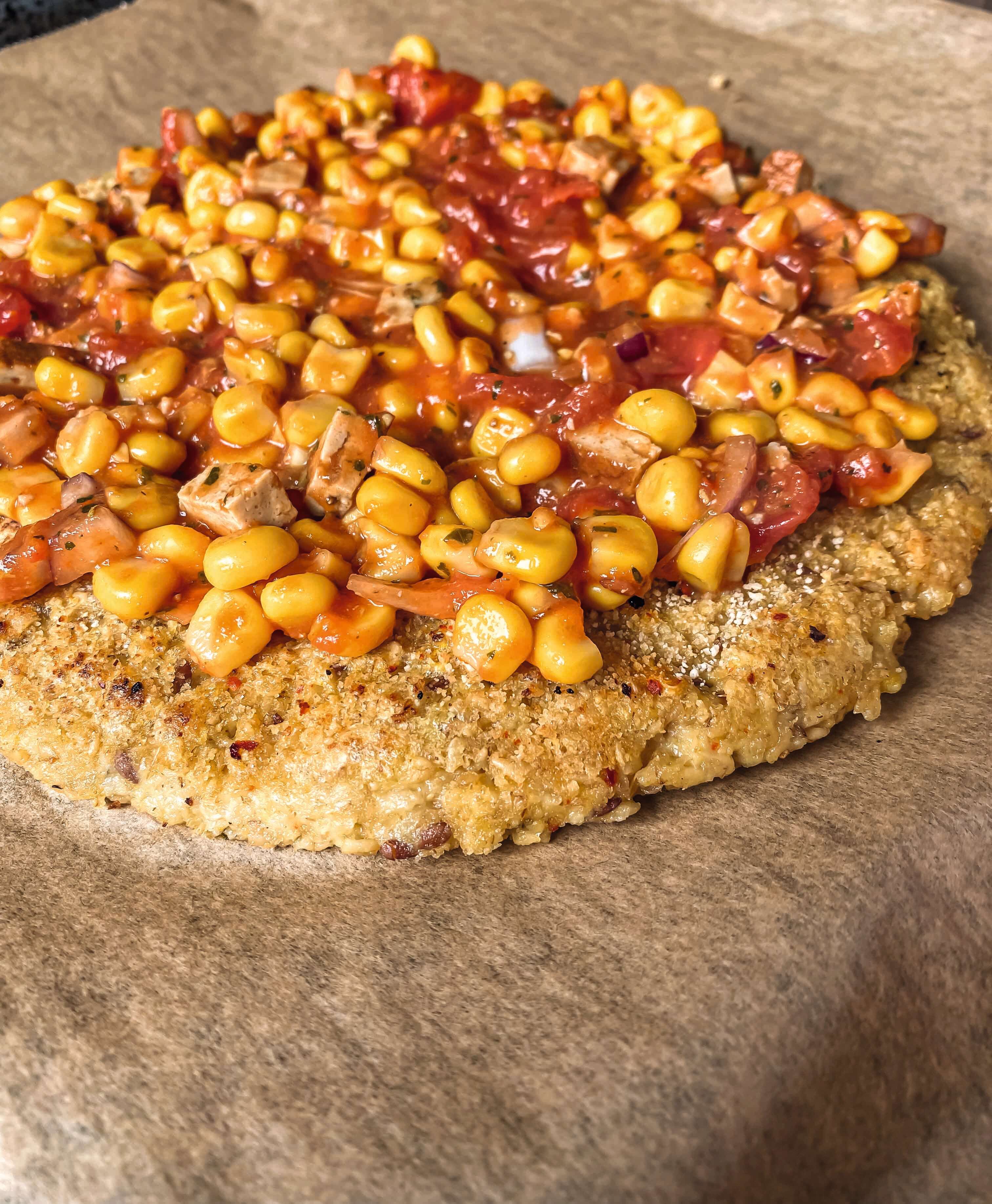 Belegen Sie die Pizza nachdem Sie die Tomatenmasse auf dem Hafer-Flockenteig verteilt haben mit dem klein geschnittenen Gemüse und Tofu